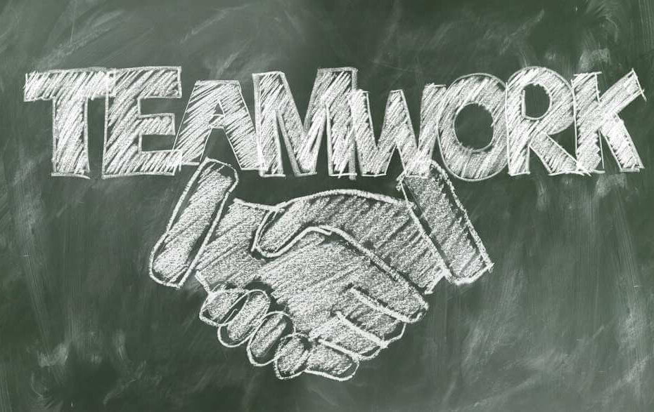 Das Wort Teamwork und zwei sich schüttelnde Hände sind auf einer Tafel abgebildet.