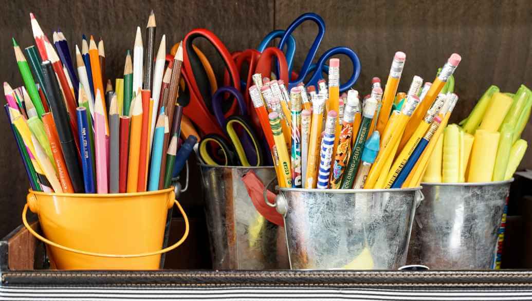 Many pencils, pens and scissors stand in four containers on a table.