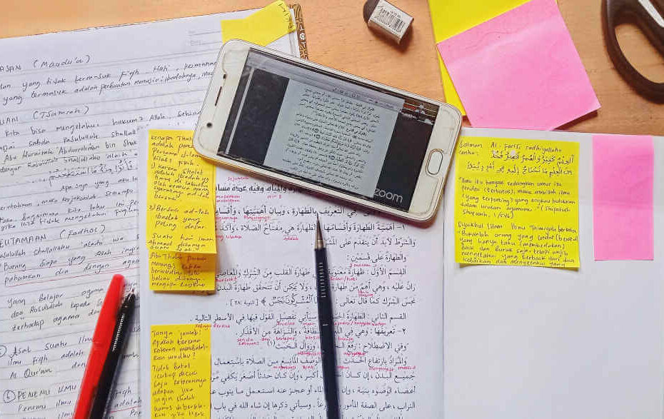 A pen, a smartphone and notebooks with sticky notes lie on a desk.