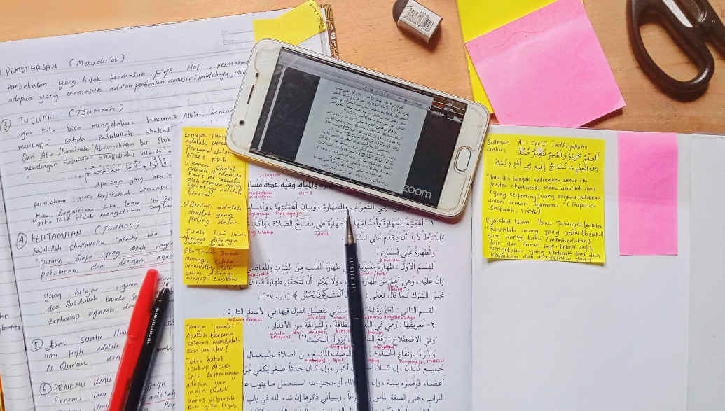 A pen, a smartphone and notebooks with sticky notes lie on a desk.