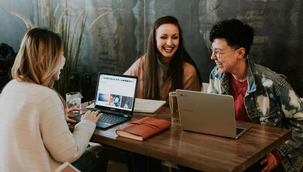 Three people are sitting at a table with their laptops and notebooks.