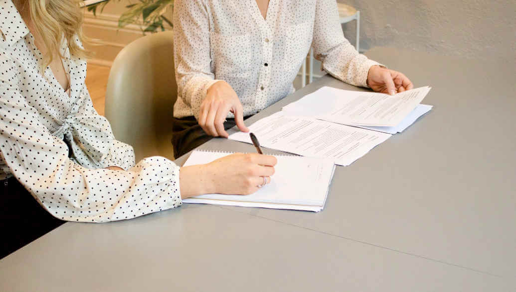 Two women are sitting at a table writing on a piece of paper.