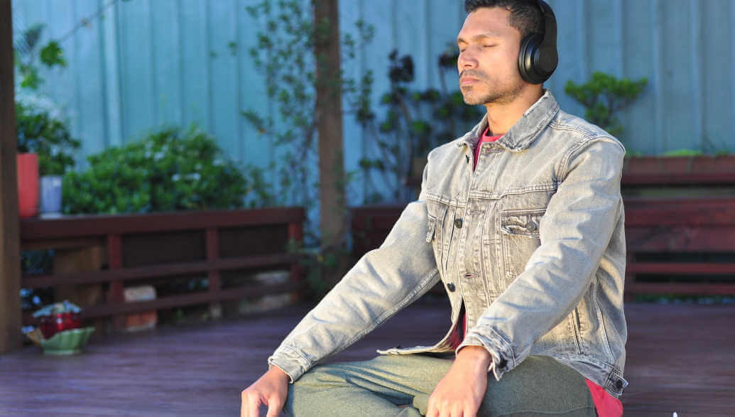 A man with headphones is sitting on a patio and is meditating.