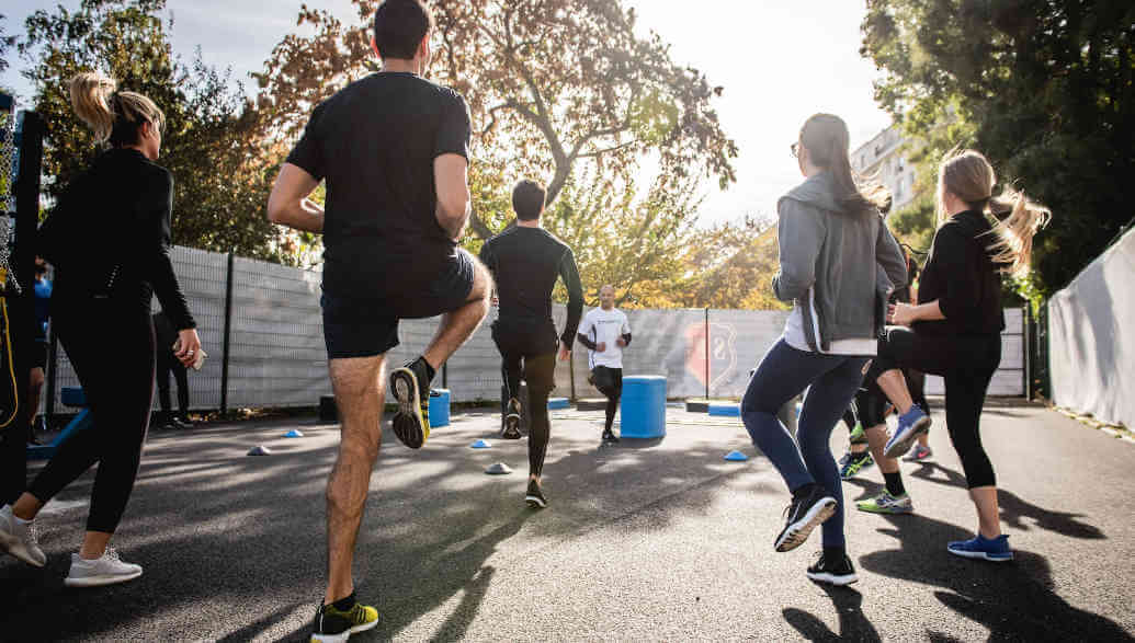 A workout group of 10 people is warming up on the street.