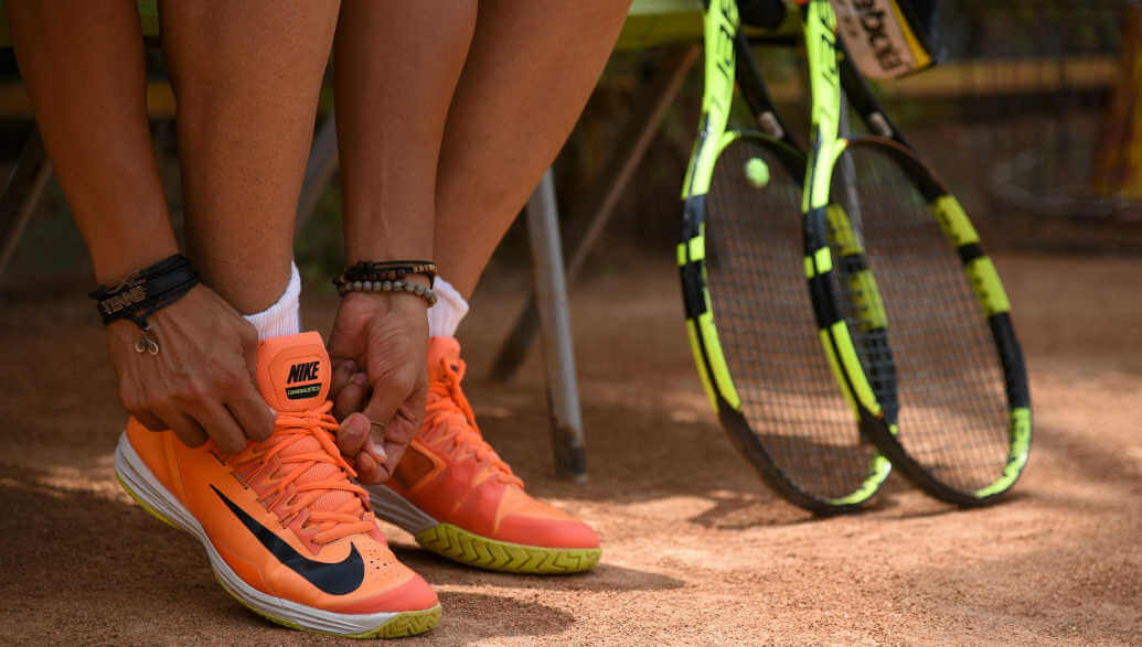 Tennis player tying his shoes next two two tennis rackets.