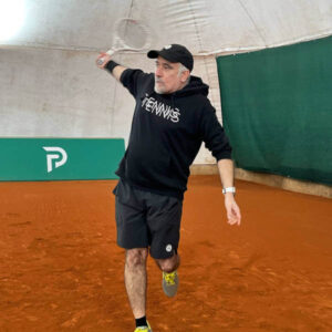 Tennistrainer Koray schlägt eine Rückhand auf einem Sandplatz.