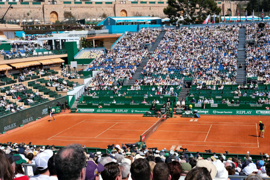 Players compete on a clay court during a sunny tournament.